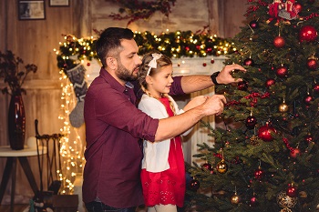 Father and daughter place an ornament on the Christmas tree